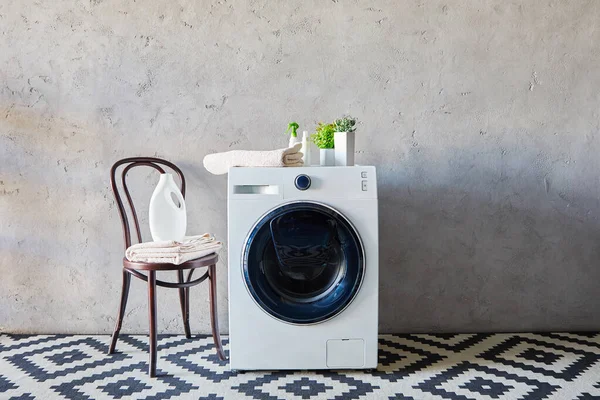 Detersivo e bottiglie spray vicino alla lavatrice, piante, asciugamani, sedia e tappeto ornamentale in bagno — Foto stock