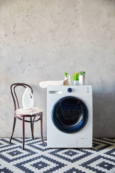Пляшка миючого засобу і рушник на стільці поруч з пральною машиною та декоративним килимом у ванній — стокове фото