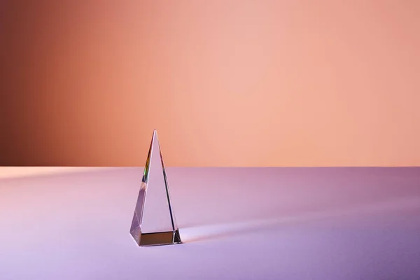 Kristall transparente Pyramide mit Lichtreflexion auf violettem und orangefarbenem Hintergrund — Stockfoto