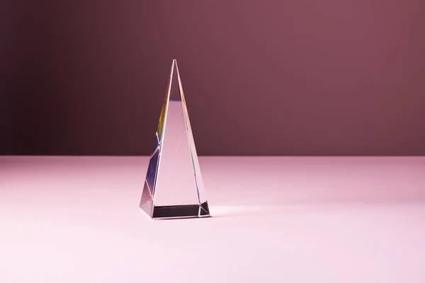 Pirâmide transparente de cristal com reflexão de luz sobre fundo rosa — Fotografia de Stock