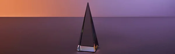 Crystal transparent pyramid with light reflection on dark purple background, horizontal crop — Stock Photo