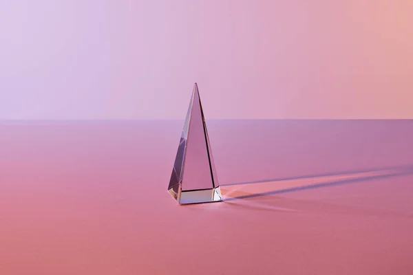 Crystal transparent pyramid with light reflection on pink background — Stock Photo