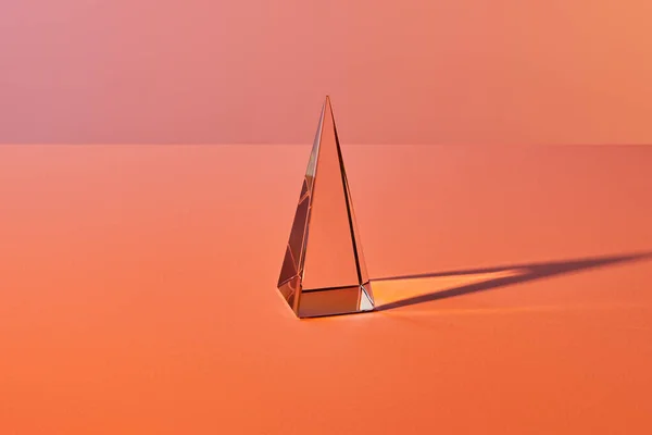 Crystal transparent pyramid with light reflection on orange background — Stock Photo