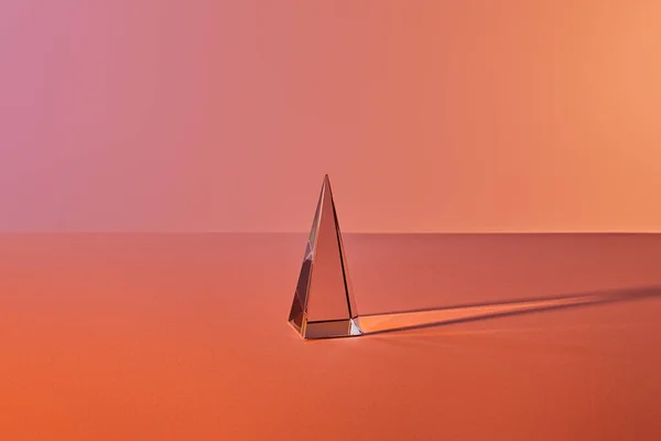 Piramide trasparente cristallo con riflesso di luce su sfondo arancione — Foto stock