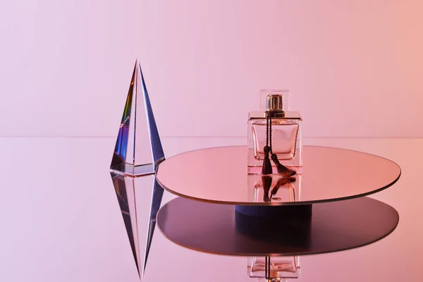 Pyramide transparente cristal avec reflet près du flacon de parfum sur miroir rond sur fond rose — Photo de stock