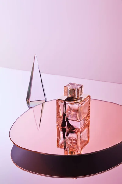 Pirâmide transparente de cristal com reflexão perto de frasco de perfume no espelho redondo no fundo rosa — Fotografia de Stock