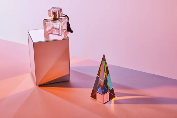 Pirâmide transparente de cristal perto de frasco de perfume no cubo sobre fundo rosa — Fotografia de Stock