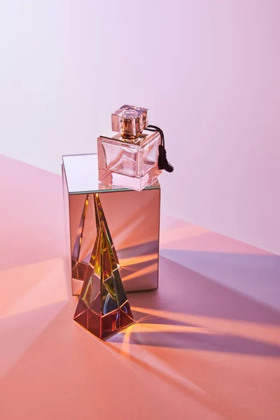 Crystal transparent pyramid near perfume bottle on cube on pink background — Stock Photo