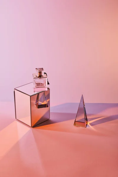 Crystal transparent pyramid near perfume bottle on cube on pink background — Stock Photo