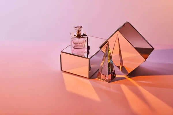 Прозрачная пирамида рядом с парфюмерной бутылкой и зеркальными кубиками на розовом фоне — стоковое фото