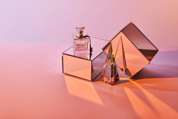 Pirâmide transparente de cristal perto de garrafa de perfume e cubos de espelho no fundo rosa — Fotografia de Stock