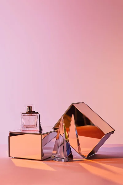 Kristall transparente Pyramide in der Nähe Parfümflasche und Spiegelwürfel auf rosa Hintergrund — Stockfoto
