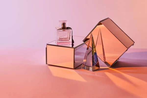 Pirâmide transparente de cristal perto de garrafa de perfume e cubos de espelho no fundo rosa — Fotografia de Stock