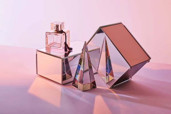 Pirâmide transparente de cristal perto de garrafa de perfume e cubos de espelho no fundo rosa — Fotografia de Stock