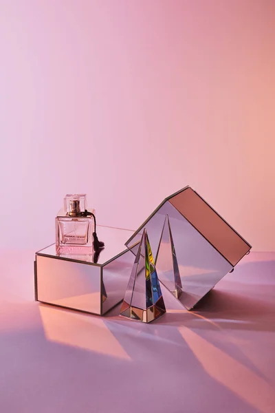 Kristall transparente Pyramide in der Nähe Parfümflasche und Spiegelwürfel auf rosa Hintergrund — Stockfoto