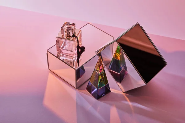 Kristall transparente Pyramide in der Nähe Parfümflasche und Spiegelwürfel auf rosa Hintergrund — Stockfoto