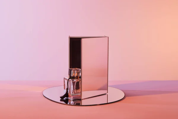 Perfume bottle on round mirror with cube on pink background — Stock Photo