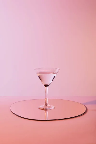 Cocktail glass with liquid on mirror with reflection on pink background — Stock Photo