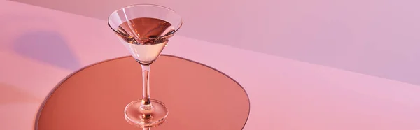 Cocktail glass with liquid on mirror with reflection on pink background, panoramic crop — Stock Photo
