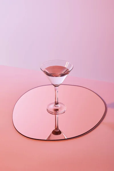 Cocktail glass with liquid on mirror with reflection on pink background — Stock Photo