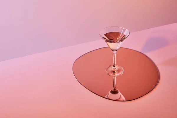 Cocktail glass with liquid on mirror with reflection on pink background — Stock Photo