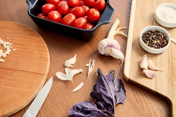 Hochwinkelansicht des Behälters mit Tomaten, Messer und Schneidebrettern mit Zutaten auf Holzgrund — Stockfoto