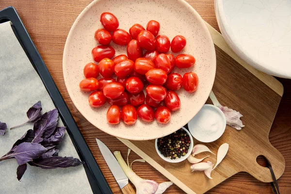 Top view of oven tray, plate and cutting board with ingredients near knife and bowl on wooden background — Stock Photo