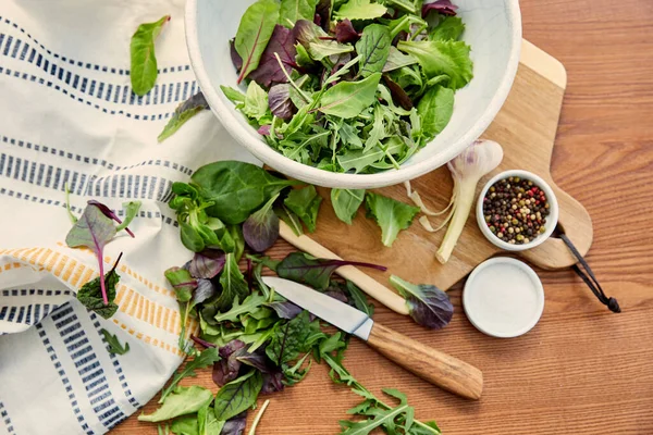 Vista dall'alto di ciotole con pepe, sale e ingredienti sul tagliere vicino a coltello e tovagliolo su sfondo di legno — Foto stock