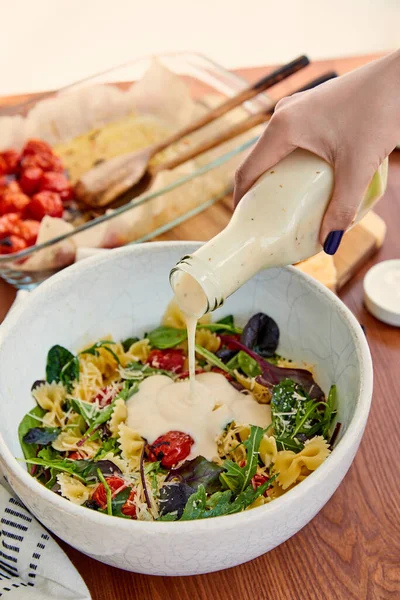 Vue recadrée de la femme versant de la mayonnaise à la salade de pâtes dans un bol sur une table isolée sur beige — Photo de stock