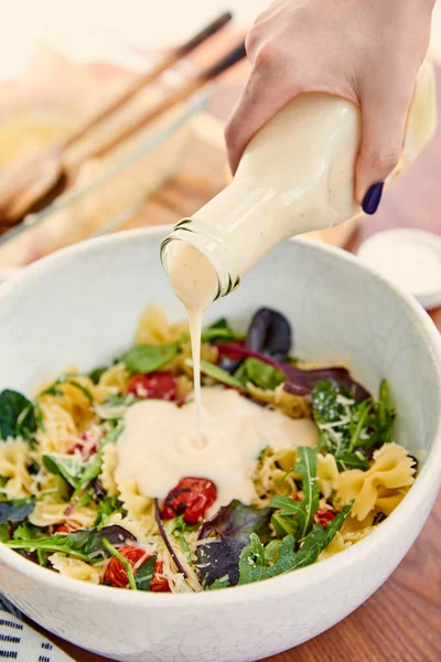 Cropped view of woman pouring mayonnaise to pasta salad in bowl on wooden and beige — Stock Photo
