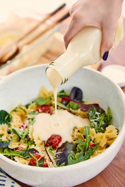 Vista ritagliata di donna versando maionese per insalata di pasta in ciotola su legno e beige — Foto stock