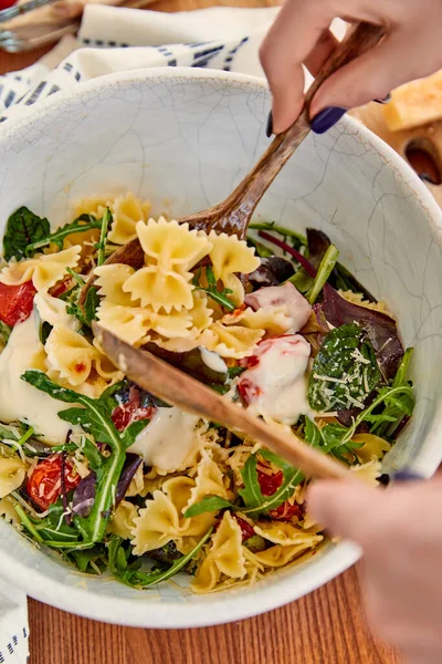 Cropped view of woman mixing pasta salad with mayonnaise in bowl near napkin on wooden background — Stock Photo