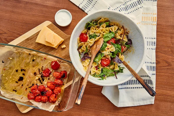 Top view of bowl with pasta salad and ingredients on cutting board near napkin on wooden background — Stock Photo