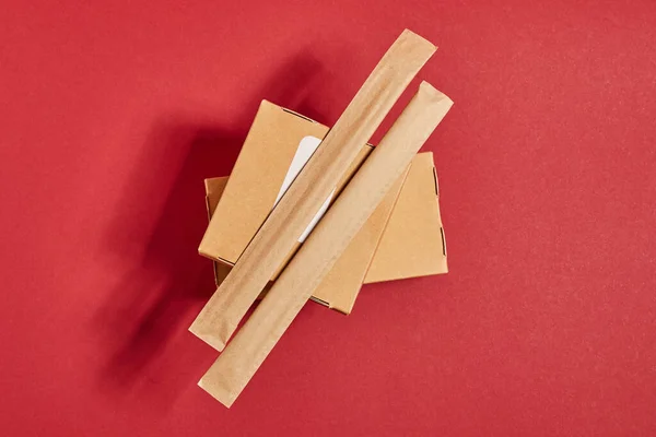 Top view of chopsticks in paper packaging on carton boxes with chinese food on red — Stock Photo