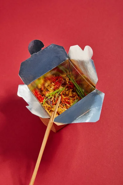 Top view of wooden chopsticks near tasty noodles with vegetables in takeaway box on red — Stock Photo