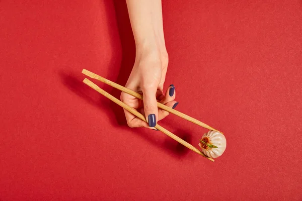 Top view of woman holding chopsticks with steamed bun on red — Stock Photo