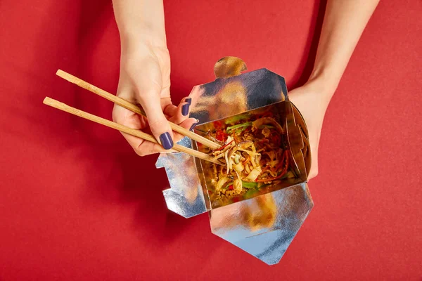 Top view of woman holding wooden chopsticks near tasty noodles on red — Stock Photo