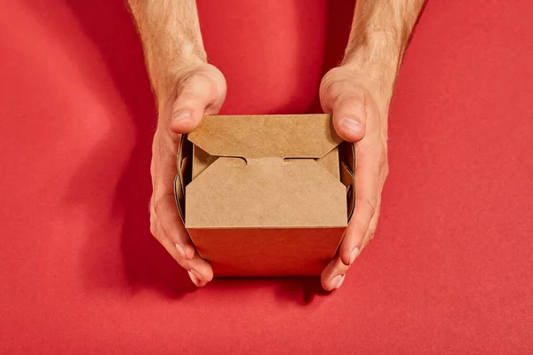 Vista superior del hombre sosteniendo caja de comida para llevar de cartón en rojo - foto de stock