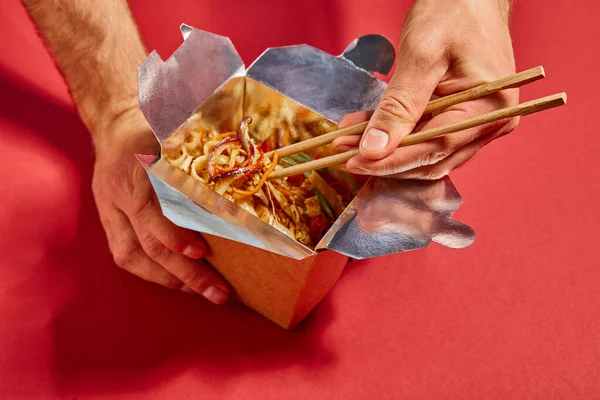 Vista recortada del hombre sosteniendo palillos cerca de sabrosos fideos en rojo - foto de stock