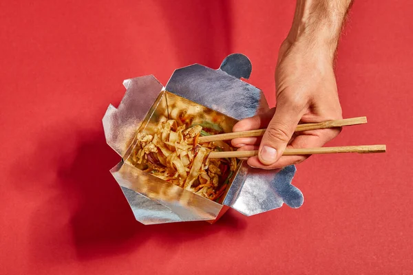 Cropped view of man holding chopsticks near spicy noodles on red — Stock Photo