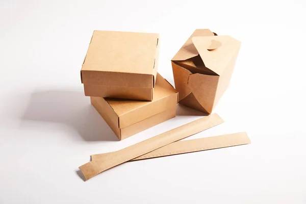 Chopsticks in paper packaging near takeaway boxes with chinese food on white — Stock Photo