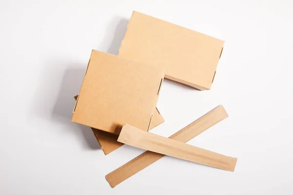Baguettes de vue en haut dans l'emballage en papier près des boîtes à emporter avec de la nourriture chinoise sur blanc — Photo de stock