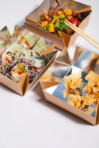 Boîtes à emporter avec des plats chinois savoureux et préparés près de baguettes sur blanc — Photo de stock