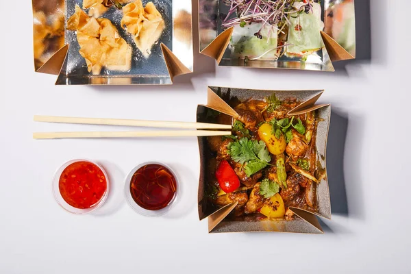 Vue du dessus des sauces et baguettes près des boîtes à emporter avec de la nourriture chinoise préparée sur blanc — Photo de stock