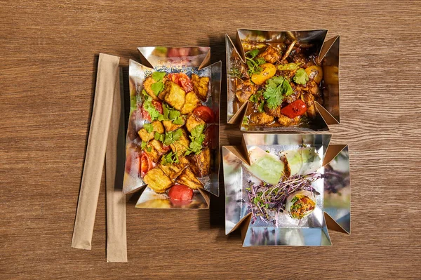 Top view of chopsticks in paper packaging near takeaway boxes with prepared chinese food on wooden surface — Stock Photo