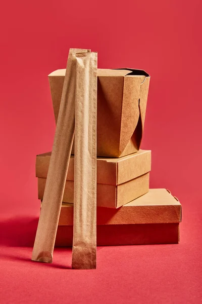 Chopsticks in paper packaging near takeaway boxes with chinese food on red — Stock Photo