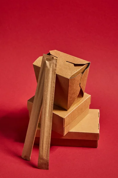 Palillos en el embalaje de papel cerca de cajas de comida para llevar con comida china preparada en rojo - foto de stock