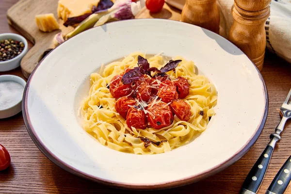 Delicious pasta with tomatoes, basil and parmesan served in round plate on wooden table in sunlight — Stock Photo