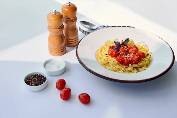 Deliciosa massa com tomate servido com talheres, moinhos de sal e pimenta na mesa branca à luz do sol — Fotografia de Stock