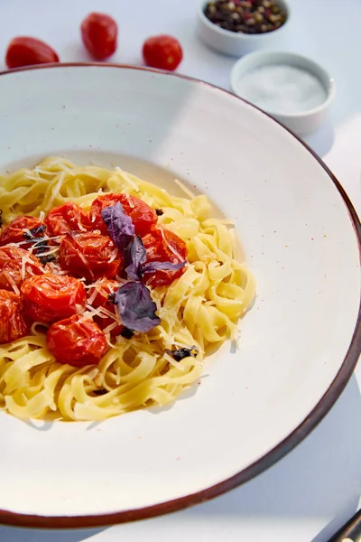 Selektiver Schwerpunkt köstlicher Pasta mit Tomaten, serviert mit Salz und Pfeffer auf weißem Tisch im Sonnenlicht — Stockfoto